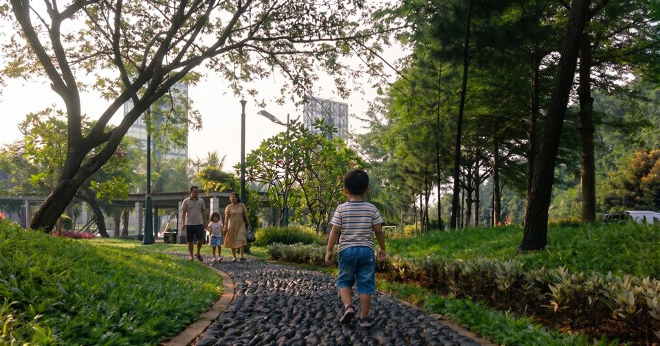 A family walks a stone path through a green, tree-filled city park at golden hour.